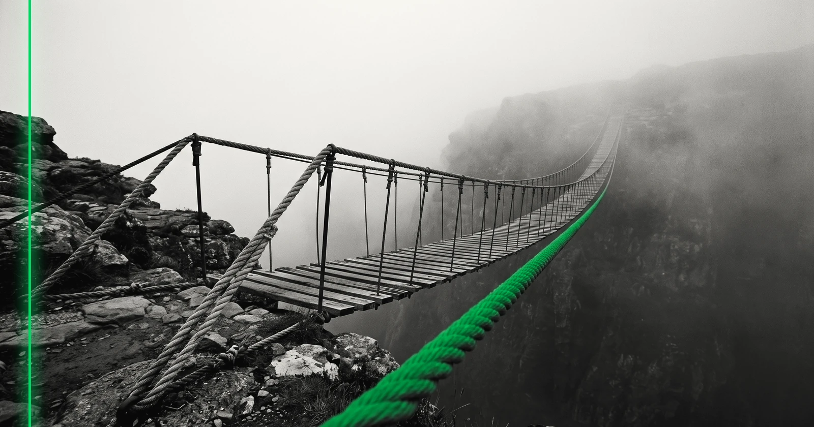Une longue passerelle suspendue traverse une vallée dans la brume, l'autre rive se perd dans le brouillard.