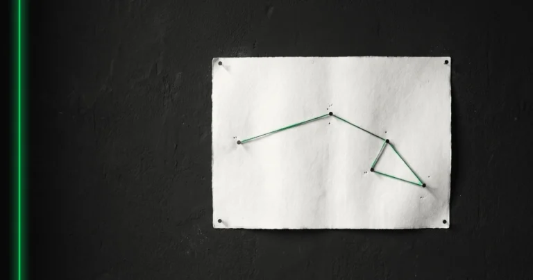 Une carte vierge épinglée au mur, un fil tendu relie les épingles et trace un itinéraire.