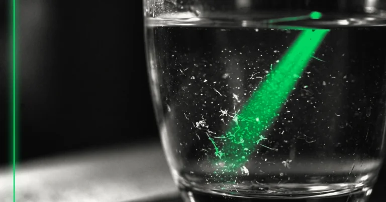 Gros plan sur un verre d'eau limpide en apparence, des particules en suspension révélées par la lumière.