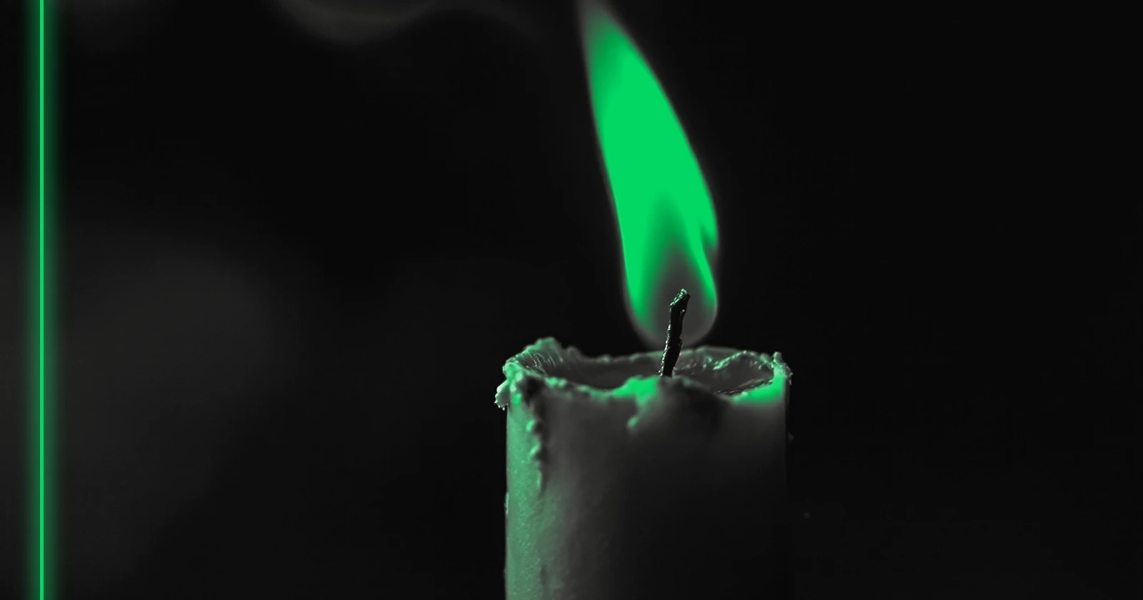 Gros plan sur une mèche de bougie presque consumée, une petite flamme et un mince filet de fumée.