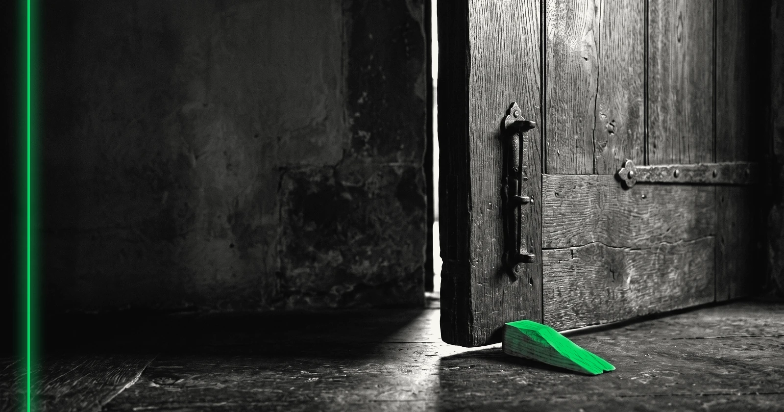 Une lourde porte en bois maintenue presque close par une cale, un fin rai de lumière passe.